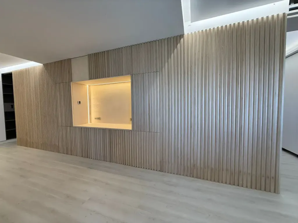 Frente continuo de listones de madera a medida con hueco iluminado que integra la cocina en una vivienda de Madrid