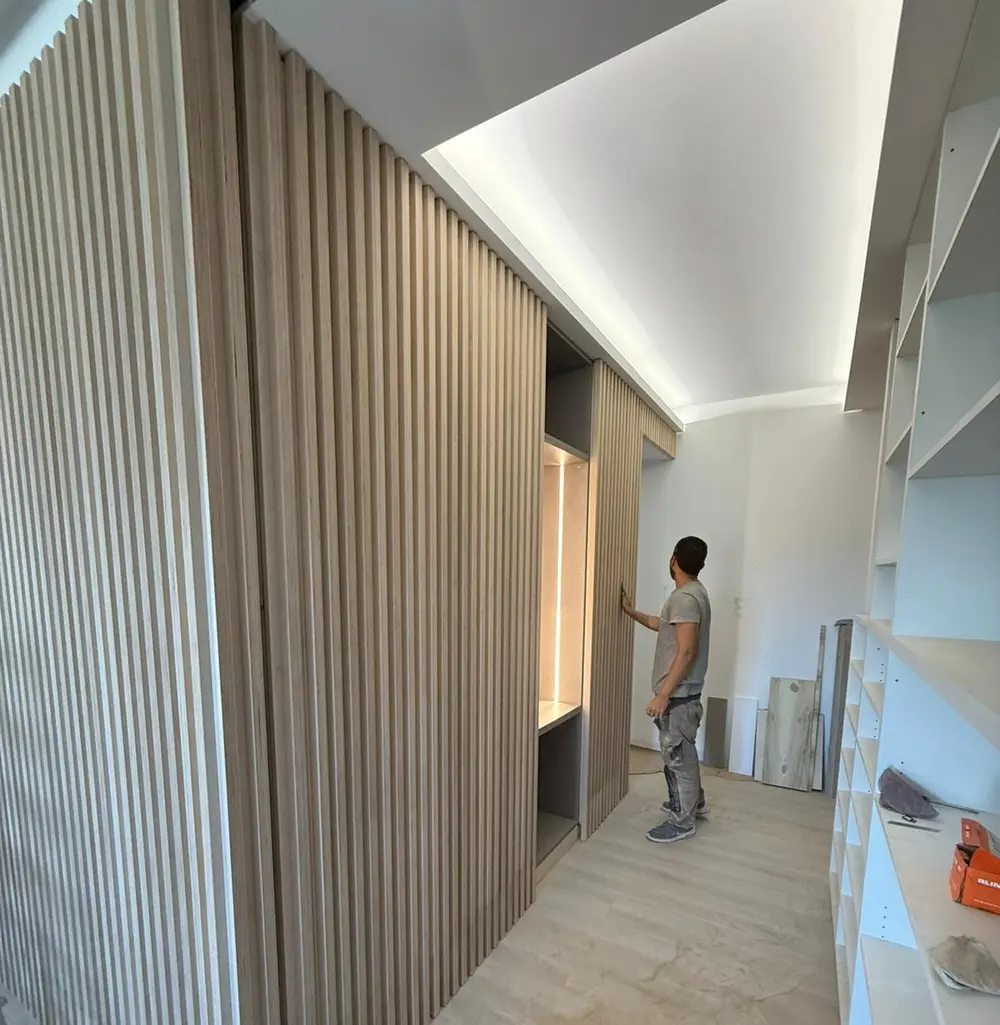 Carpintero deslizando una puerta corredera oculta integrada en un frente de listones de madera a medida en Madrid